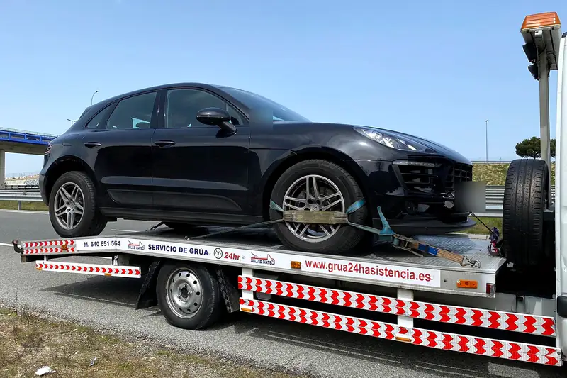 Asistencia en carretera: grúa con un todocamino negro cargado junto a la autovía