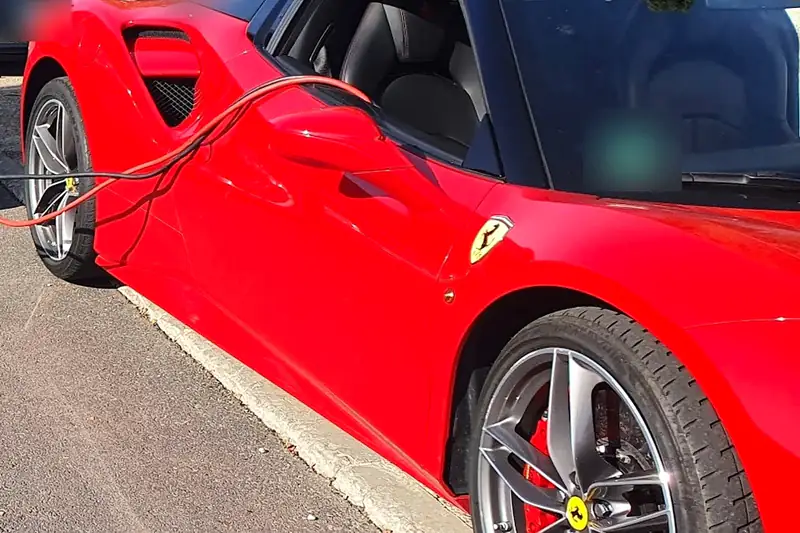 Batería del coche descargada: cables de arranque conectados a un deportivo rojo