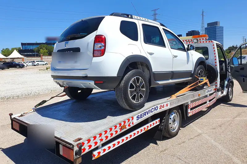 Grúa de plataforma con un todocamino blanco cargado en un aparcamiento al aire libre