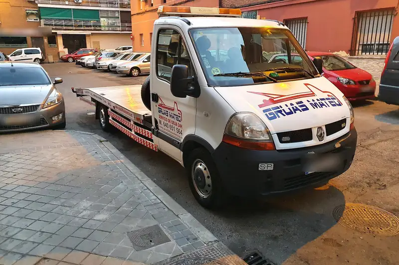 Grúa particular en una calle de barrio con edificios de ladrillo y coches aparcados
