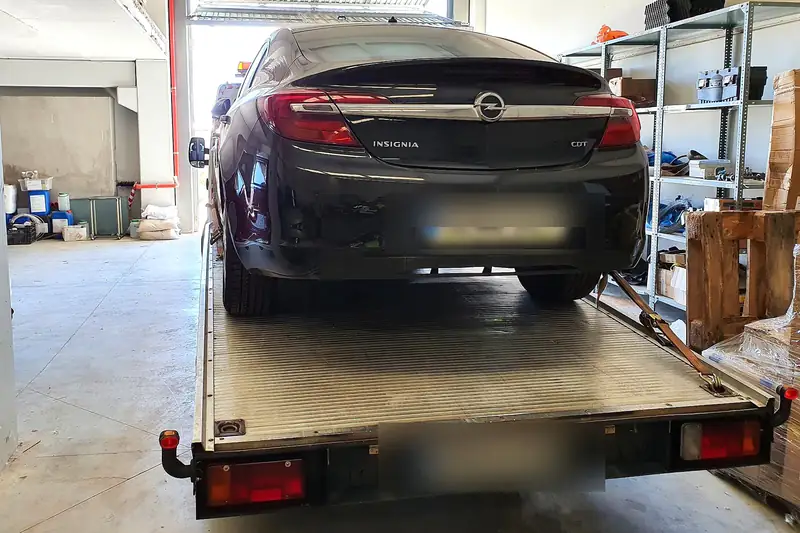 Grúa dentro de un taller mecánico con una berlina negra cargada en la plataforma