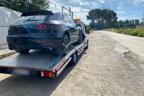 Grúa con un todocamino negro cargado, parada en el margen de una carretera