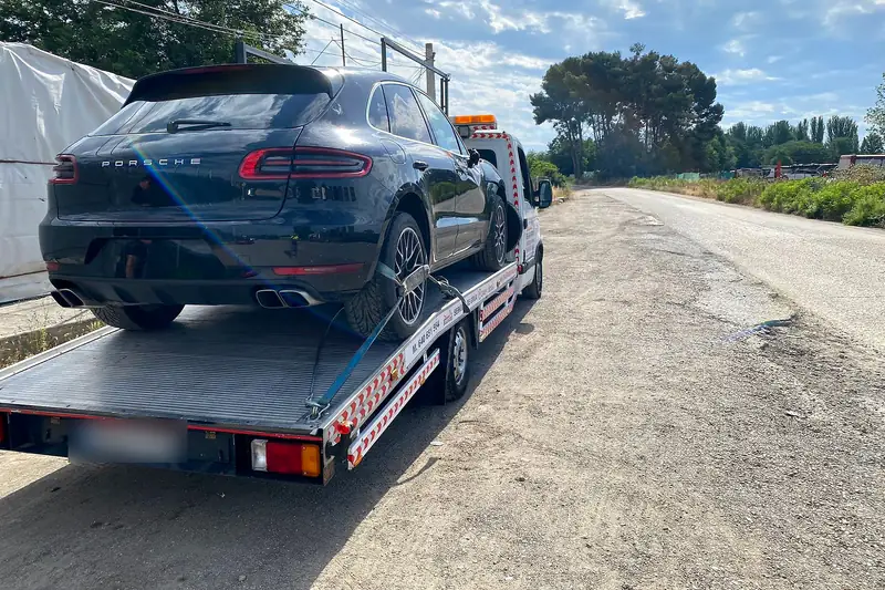Grúa con un todocamino negro cargado, parada en el margen de una carretera