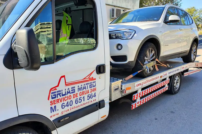 Grúa para coches con un todocamino blanco amarrado con cinchas en la plataforma