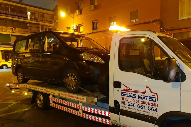 Grúa para furgonetas con una furgoneta negra cargada de noche, con la rotativa encendida