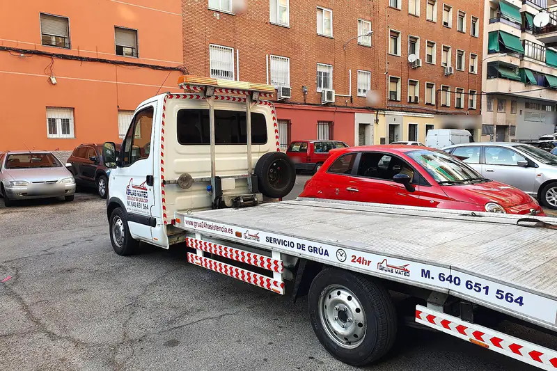 Grúa particular de plataforma en una calle de barrio con edificios de ladrillo