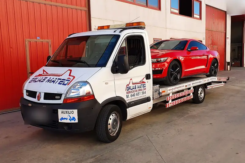 Grúa con un deportivo rojo cargado en un polígono industrial