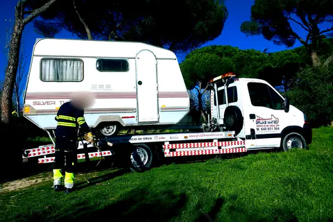 Grúa transportando una caravana mientras el operario asegura la carga