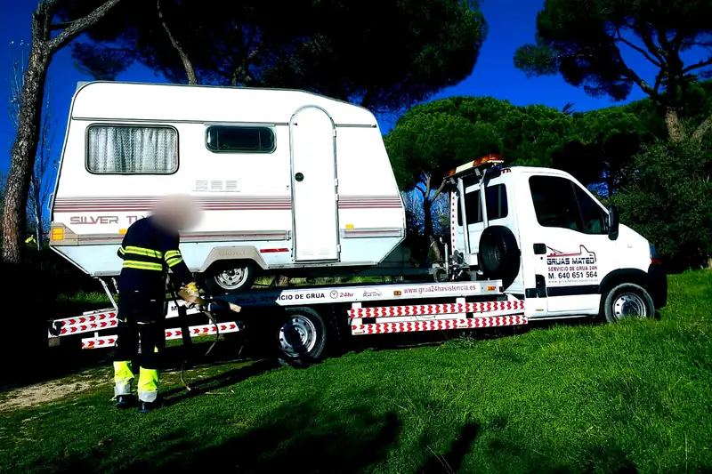 Grúa transportando una caravana mientras el operario asegura la carga