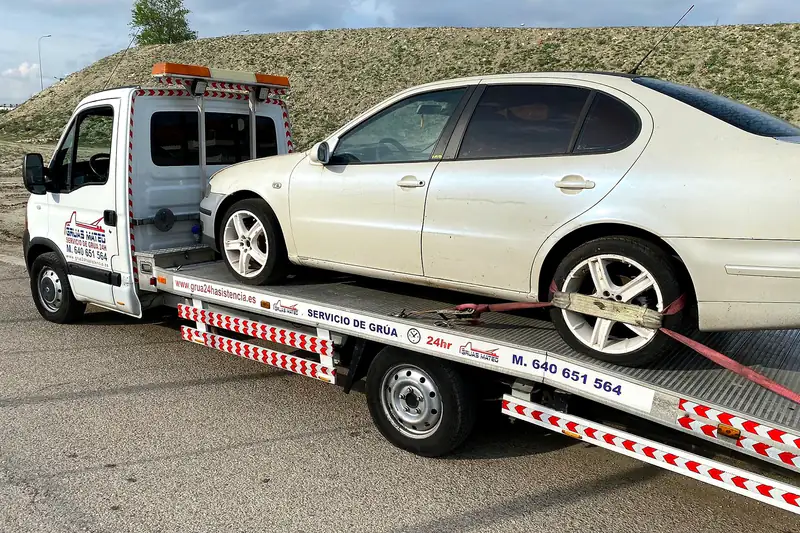 Transporte de coches: turismo blanco amarrado en la plataforma de la grúa